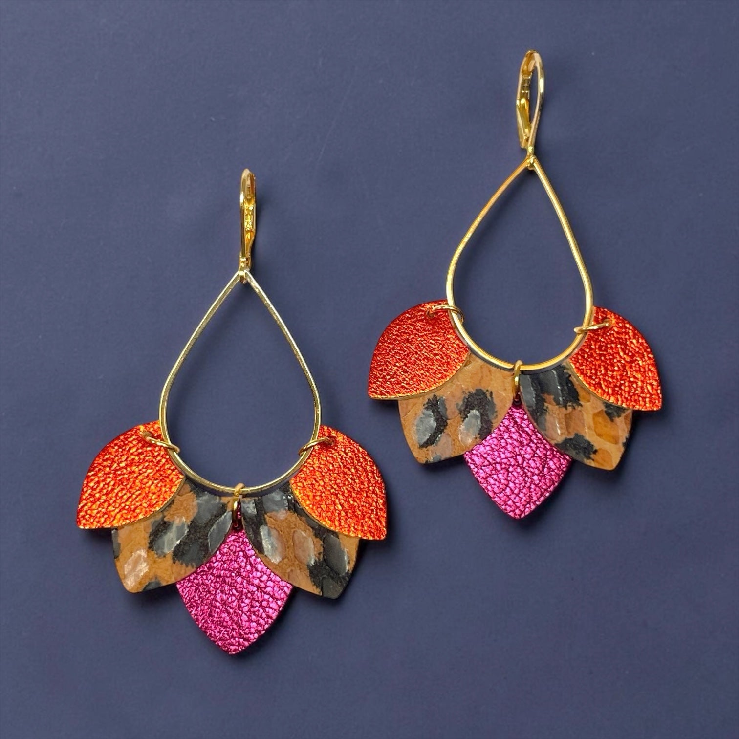 Boucles d'oreilles Nune modèle Aponi dorées à l'or fin avec pétales de cuirs orange sanguine métallisé, léopard, fushia métallisé, sur fond indigo