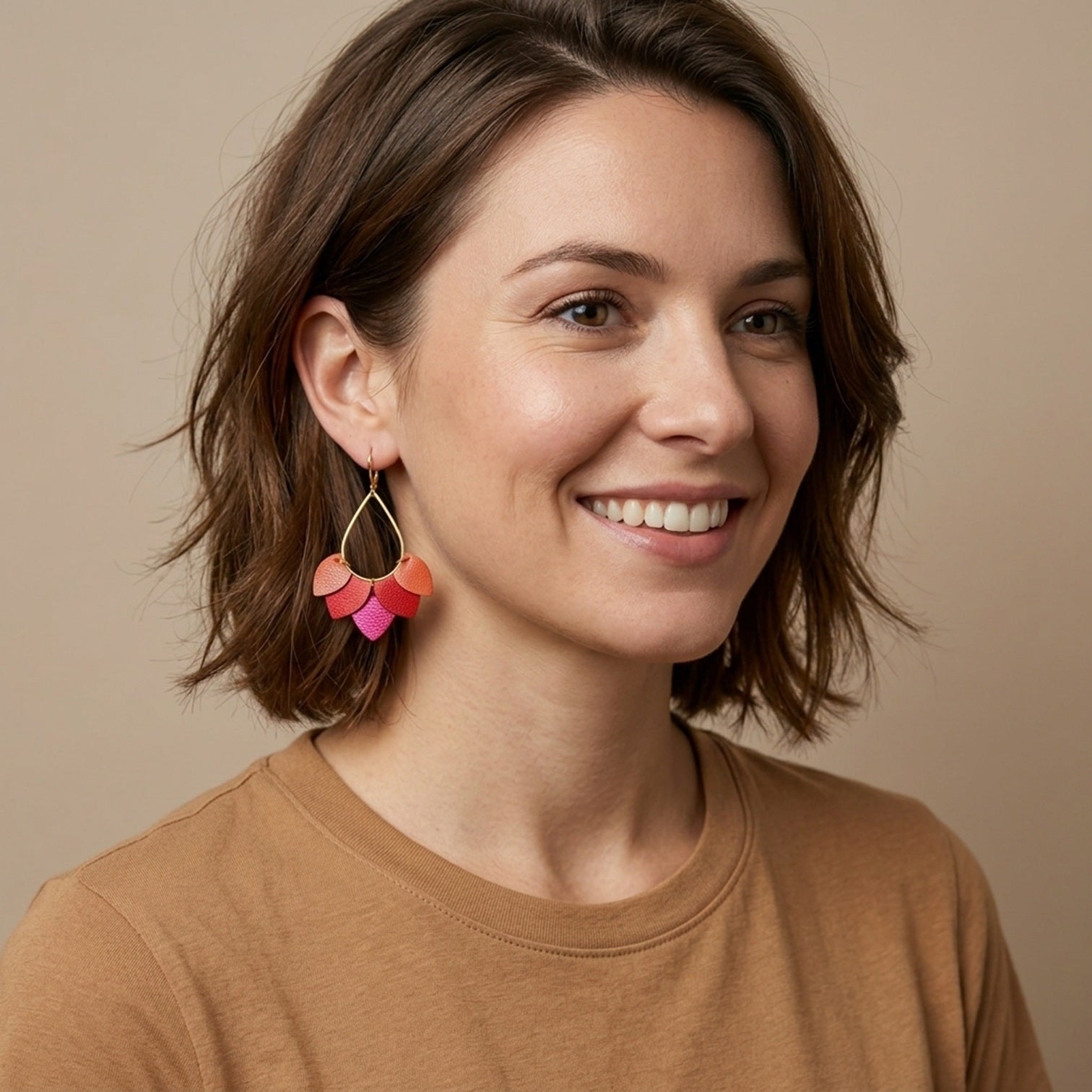 Boucles d'oreilles Nune modèle Aponi dorées à l'or fin avec pétales de cuirs corail nacré, coquelicot nacré et fushia métallisé, portées par une femme
