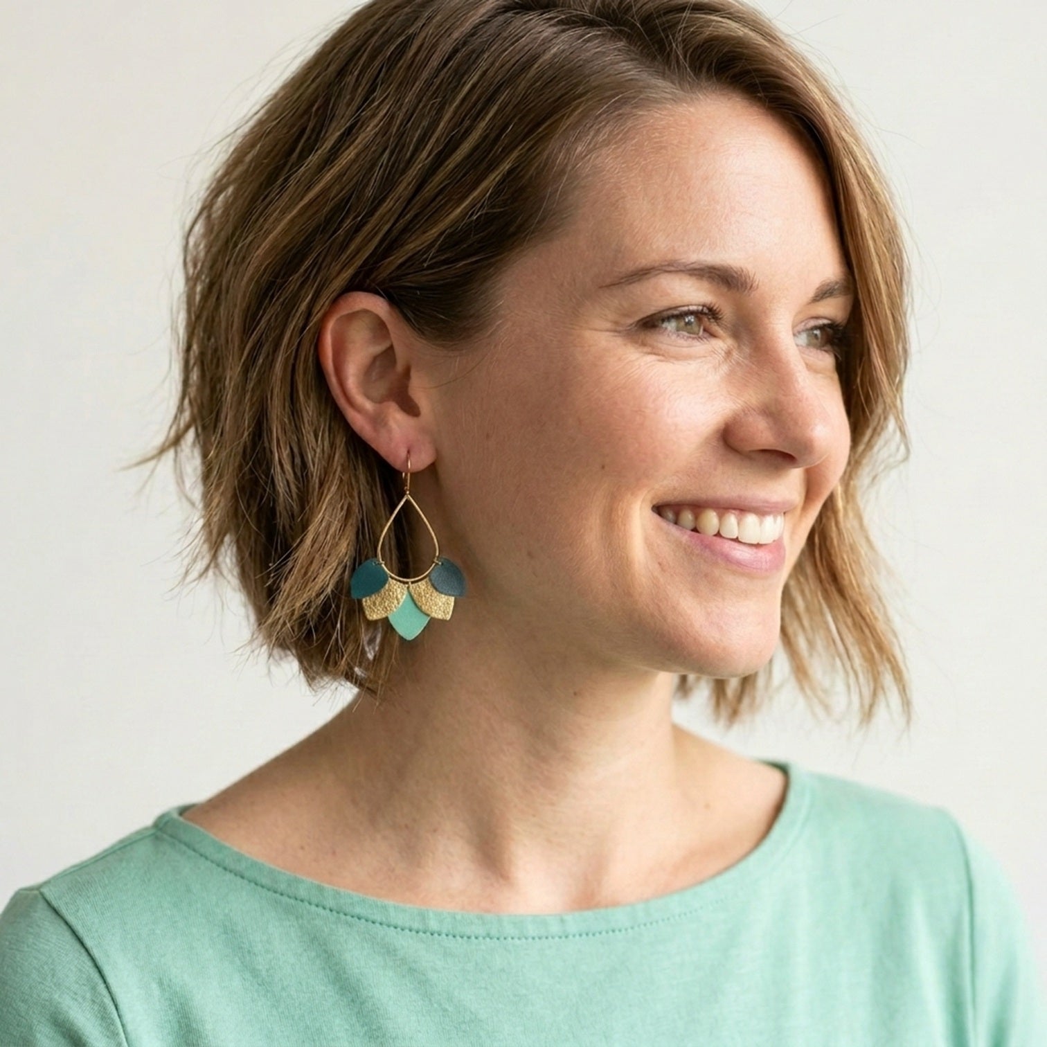 Boucles d'oreilles Nune modèle Aponi dorées à l'or fin avec pétales de cuirs vert canard, doré et menthe, portées par une femme