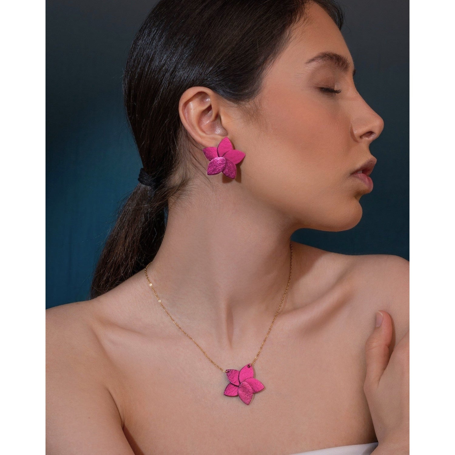 Collier doré court avec pendentif en cuir fushia métallisé en forme de fleur, porté par une femme brune portant aussi les boucles d'oreilles assorties
