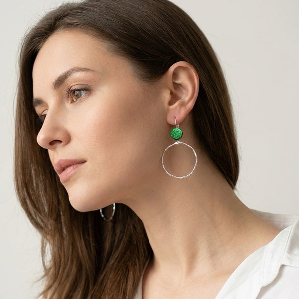 Créoles délicates martelées argentées avec pastille de cuir vert métallisé, portées aux oreilles par une femme brune