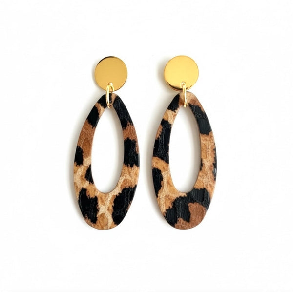 Puces d'oreilles dorées Drys de la marque Nune, avec leurs anneaux ovales en cuir léopard, sur fond blanc