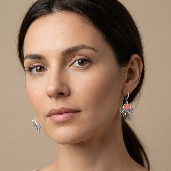 Petites boucles d'oreilles argentées Miria forme soleils avec cabochons de cuir corail nacré portées par une femme brune