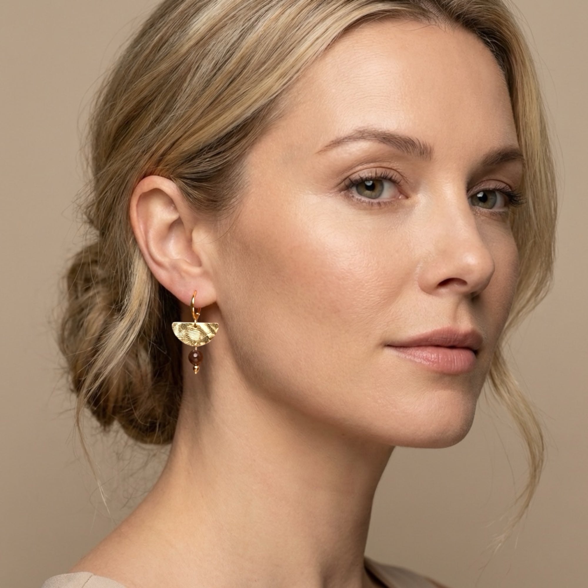 Petites boucles d'oreilles pendantes, de forme demi-lune, en métal martelé doré à l'or fin et perles de Pyrite, portées aux oreilles par une femme blonde