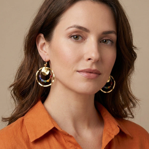 Grandes boucles d'oreilles créoles dorées pendantes longues rondes avec double anneau et petites pierres naturelles multicolores des 7 Chakras, portées aux oreilles par une femme brune