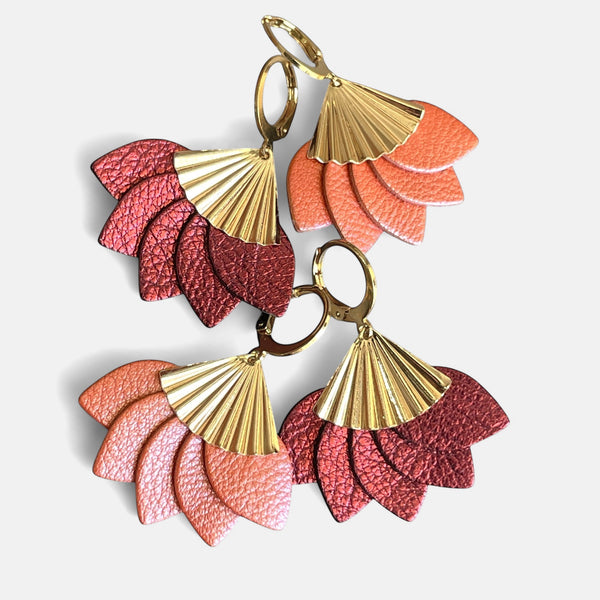 2 paires de boucles d'oreilles dorées en forme éventail en cuir recyclé corail nacré et grenat métallisé de la marque Nune modèle Sakura, sur fond de cuir blanc