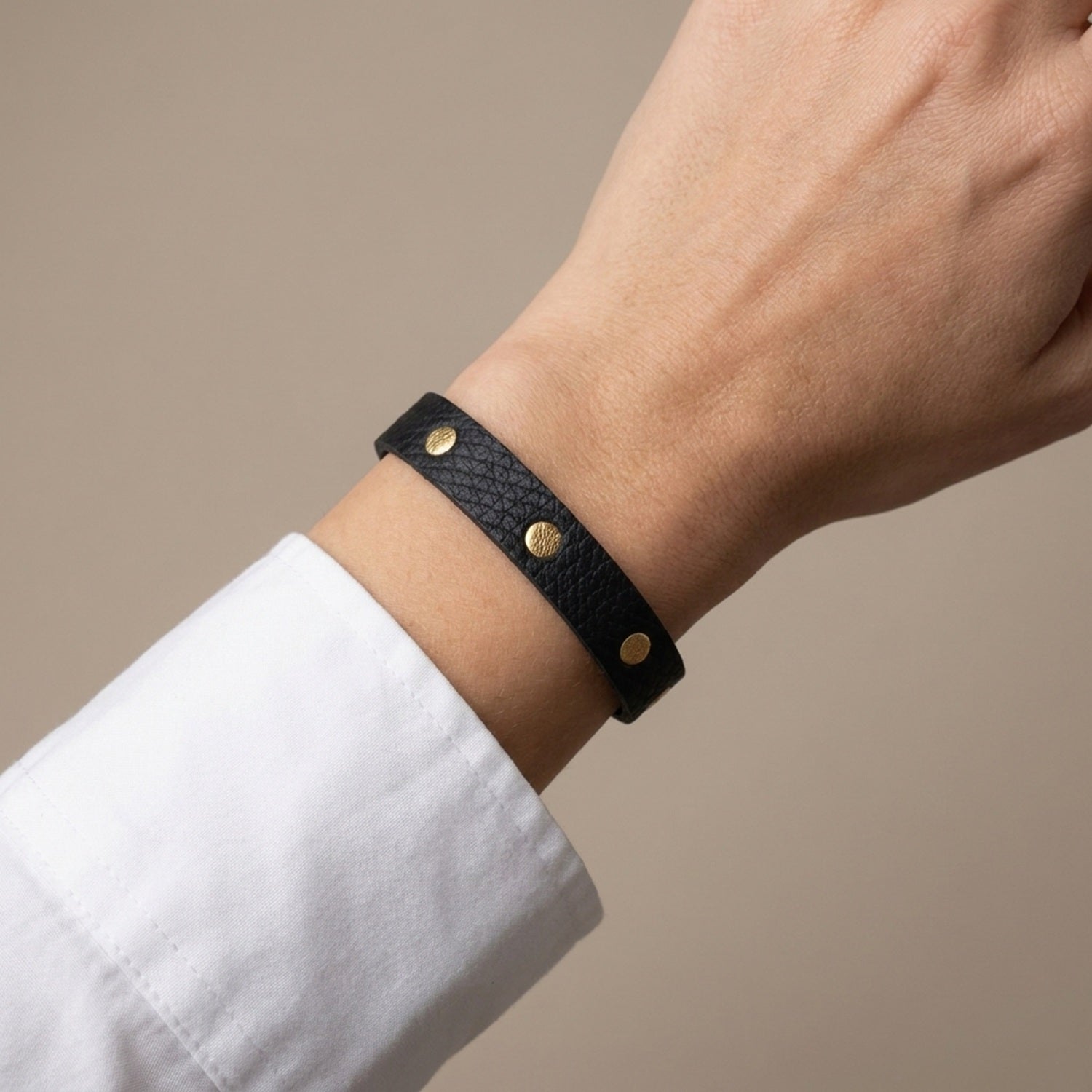 Bracelet doré en cuirs bicolore noir grainé et or, porté au poignet