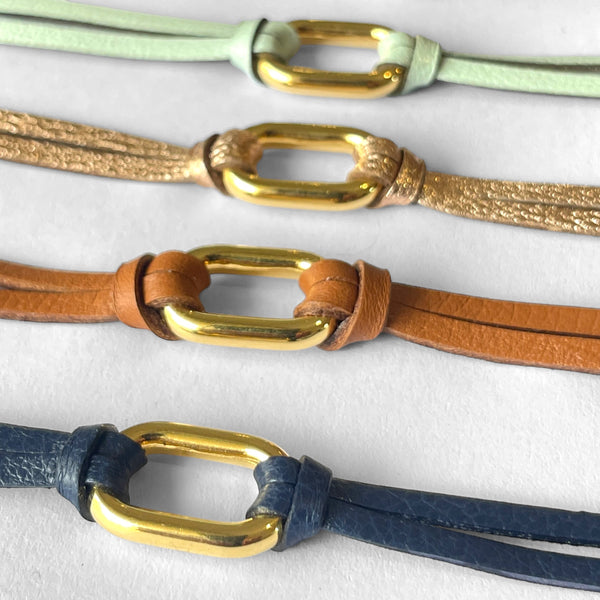 4 Bracelets à boucle dorée en fins liens de cuirs bleu marine, camel, rose pâle métallisé et vert d'eau, sur fond blanc