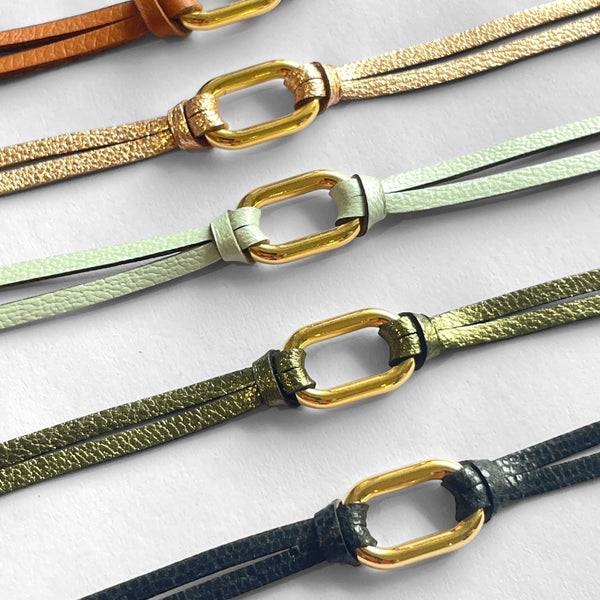 5 Bracelets à boucle dorée en fins liens de cuirs noir brillant façon serpent, camel, rose pâle métallisé, kaki métallisé et vert d'eau, sur fond blanc