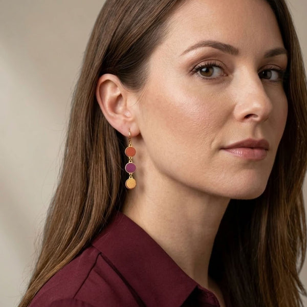 Boucles d'oreilles pendantes Cassia Nune en chapelet de trois sequins dorés et cuirs upcyclés cuivre clair, pourpre et et terracotta métallisé, portées aux oreilles
