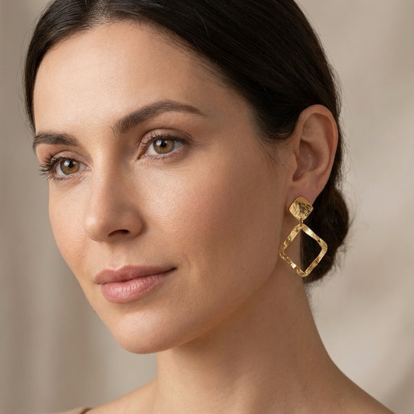 Boucles d'oreilles puces dorées à l'or fin en métal martelé avec pendentif en forme de losange, portées aux oreilles