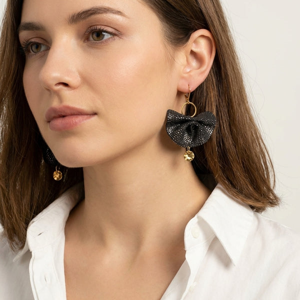 Grandes boucles d'oreilles dorées en éventails de cuir plissé recyclé bleu marine satiné, portées aux oreilles par une femme brune