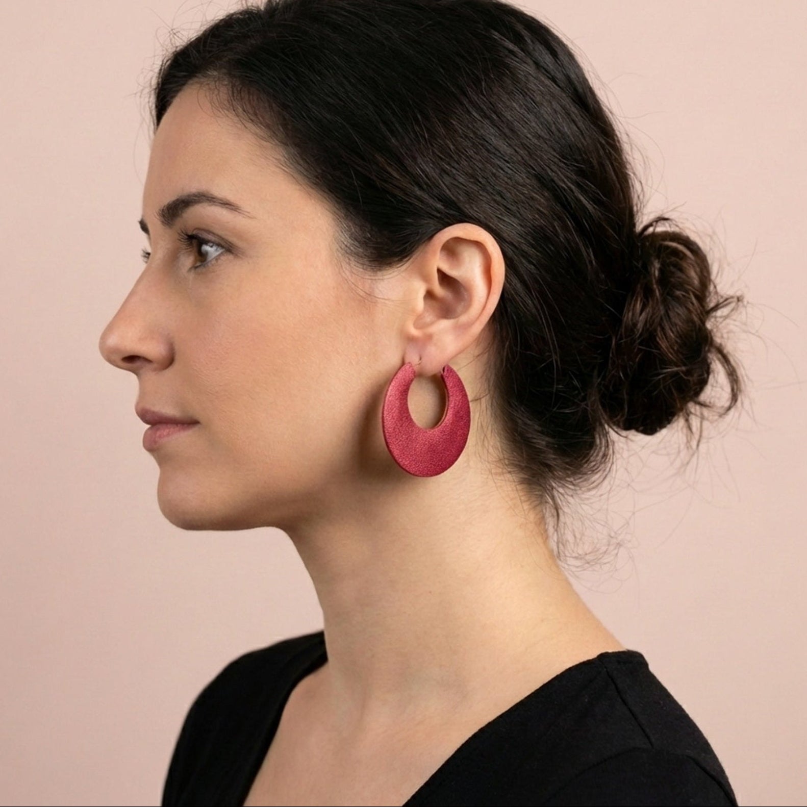 Jeune femme à chignon vue de profil portant les grandes boucles d'oreilles créoles rondes tout-cuir Circus, vues du côté rubis métallisé