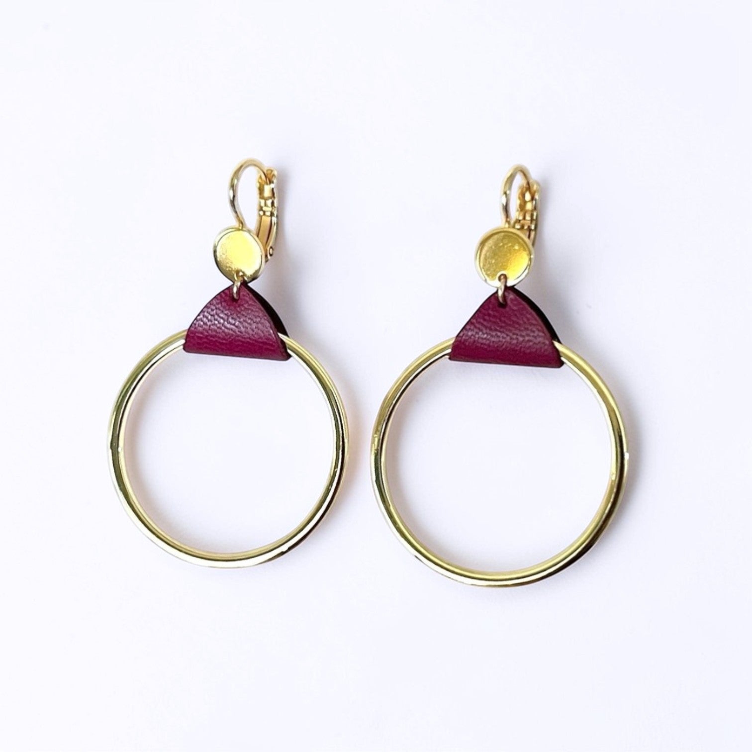 Boucles d'oreilles dorées, grands anneaux créoles, noués par un morceau de cuir pourpre aux accroches dormeuses, présentées sur fond blanc