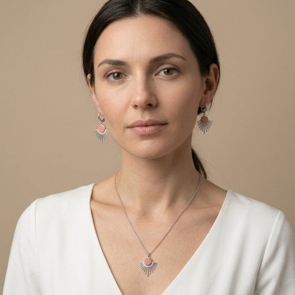 Collier argenté fin avec pendentif en forme de petit soleil, avec cabochon de cuir coloré corail nacré, porté au cou par une femme brune