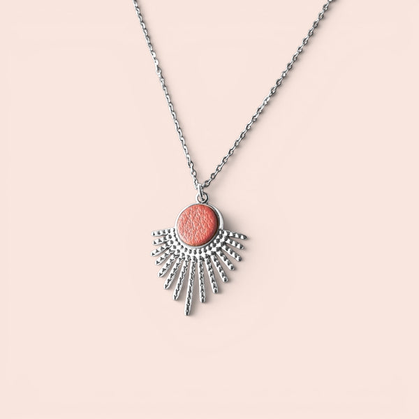 Collier argenté fin avec pendentif en forme de petit soleil, avec cabochon de cuir coloré corail nacré, sur fond rose pâle