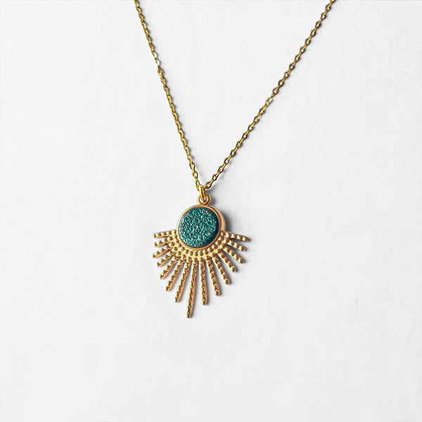 Collier doré fin avec pendentif en forme de petit soleil, avec cabochon de cuir coloré revalorisé bleu paon pailleté, sur fond blanc