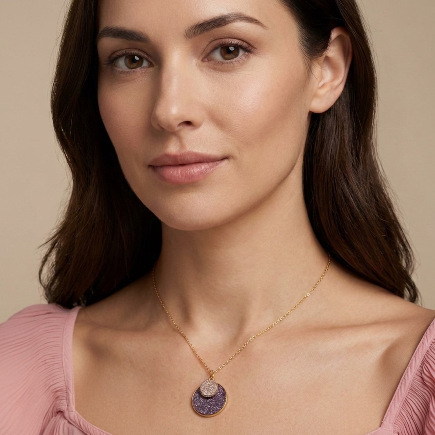Colliers Bulle pailletée Nune, court doré avec pendentif rond composé de doubles sertis de cuirs pailletés mauve et rose, porté au cou par une femme brune