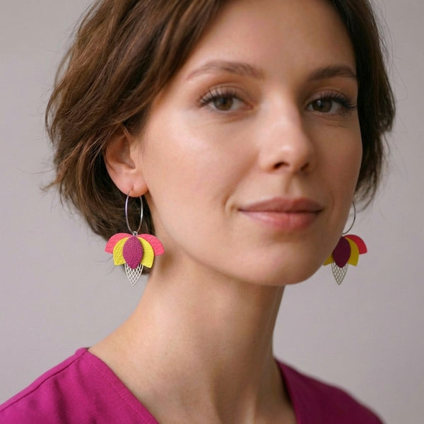 Créoles argentées en forme de fleurs de Lotus en cuirs rose fluo grainé, jaune citron et fushia métallisé, portées aux oreilles par une femme brune