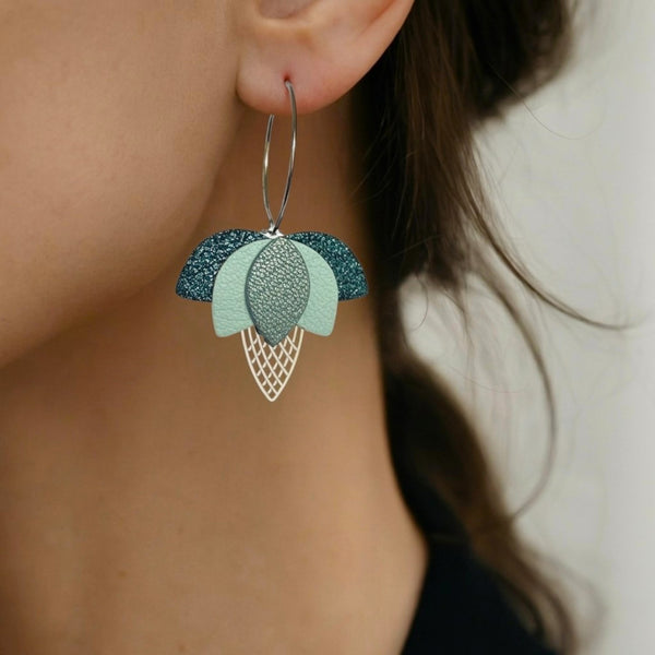 Créoles dorées en forme de fleurs de Lotus en cuirs bleu paon pailleté, bleu nuage et bleu gris nacré portées aux oreilles
