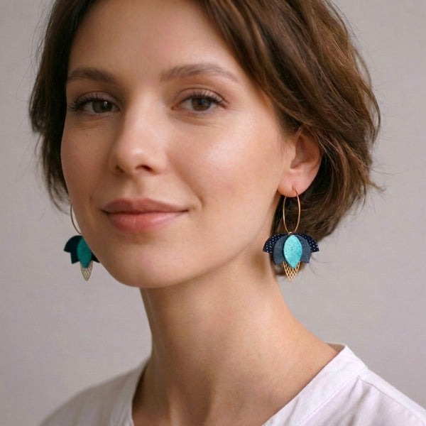 Créoles dorées Nune en forme de fleurs de Lotus en cuirs noir grainé irisé, vert sombre et vert émeraude brillant intense portées aux oreilles par une femme brune