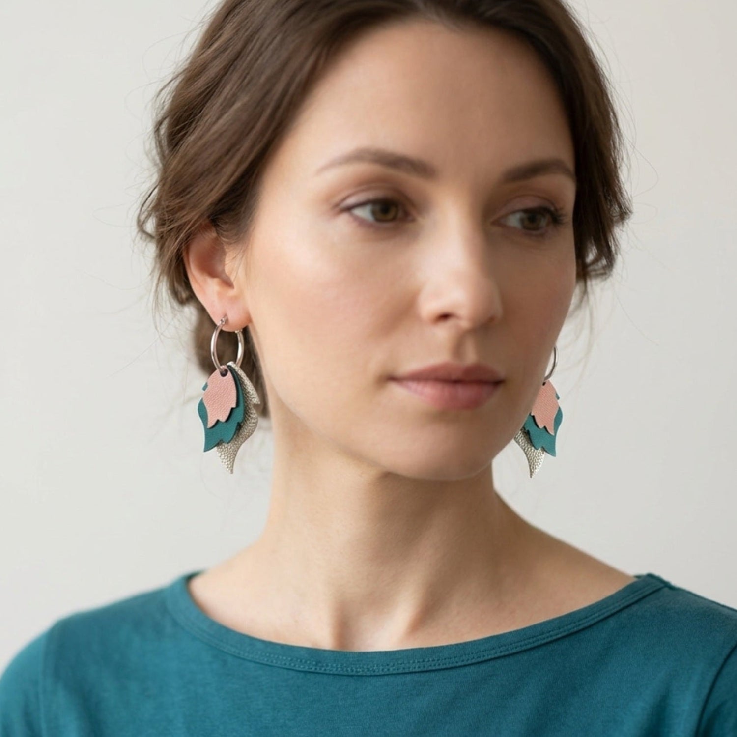 Créoles dorées avec 3 pendentifs modulables en forme de flammes en cuirs vieux rose nacré, vert canard et argent, portées à l'oreille par une femme brune