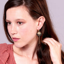 Charger l&#39;image dans la galerie, Jeune femme de profil portant les Longues boucles d&#39;oreilles dorées en forme de demi-lune en cuirs doré et noir pailleté or recyclé, sur fond mauve
