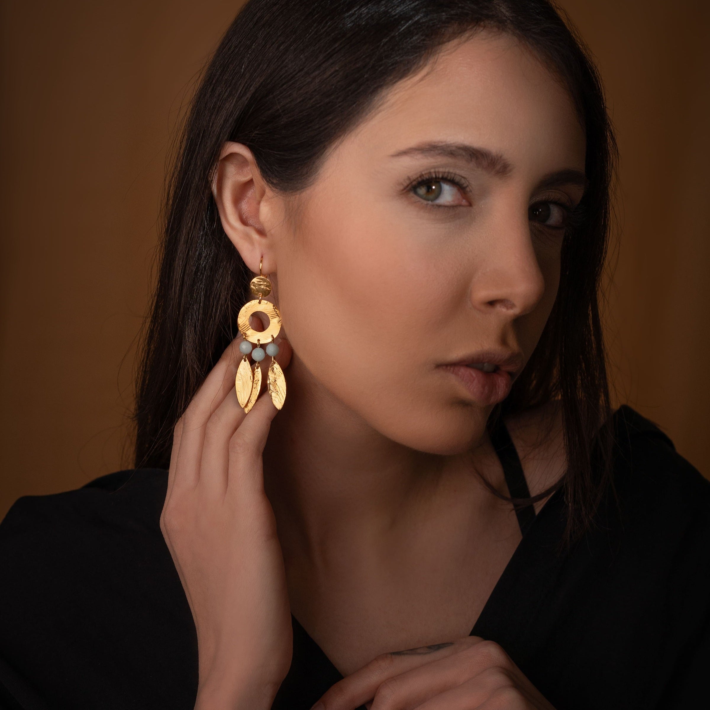 Longues boucles d'oreilles en métal martelé doré à l'or fin et perles d'amazonite de style ethnique, portées à l'oreille par une femme brune