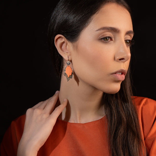 paire de Boucles d'oreilles style bohème-chic, plaquées argent, en forme de flammes en cuirs recyclés saumon clair et gris craquelé métallisé, portées à l'oreille par une femme brune