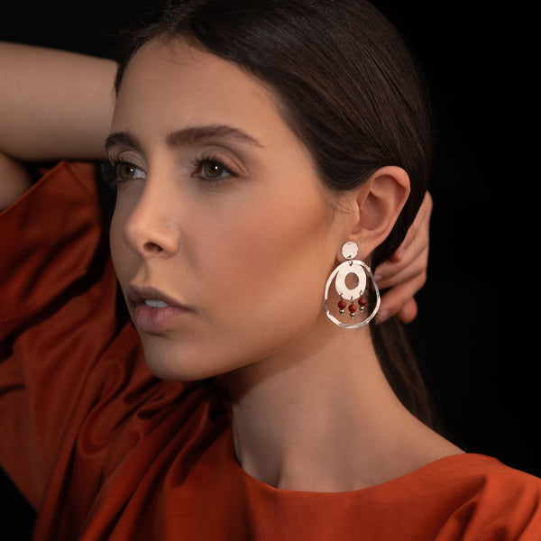 Grandes boucles d'oreilles puces créoles dorées pendantes longues rondes avec double anneau et petites perles en mokaïte acajou, portées à l'oreille par une femme brune