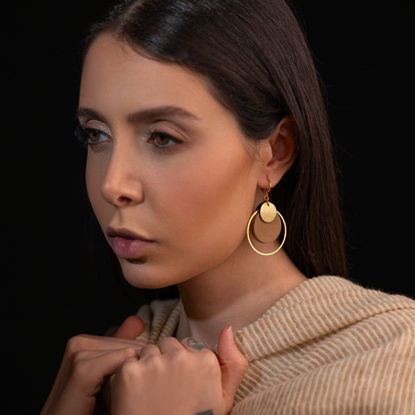 boucles d'oreilles dorées Nune modèle Danaé en cuirs beige amande et doré satiné, portées à l'oreille par une femme brune