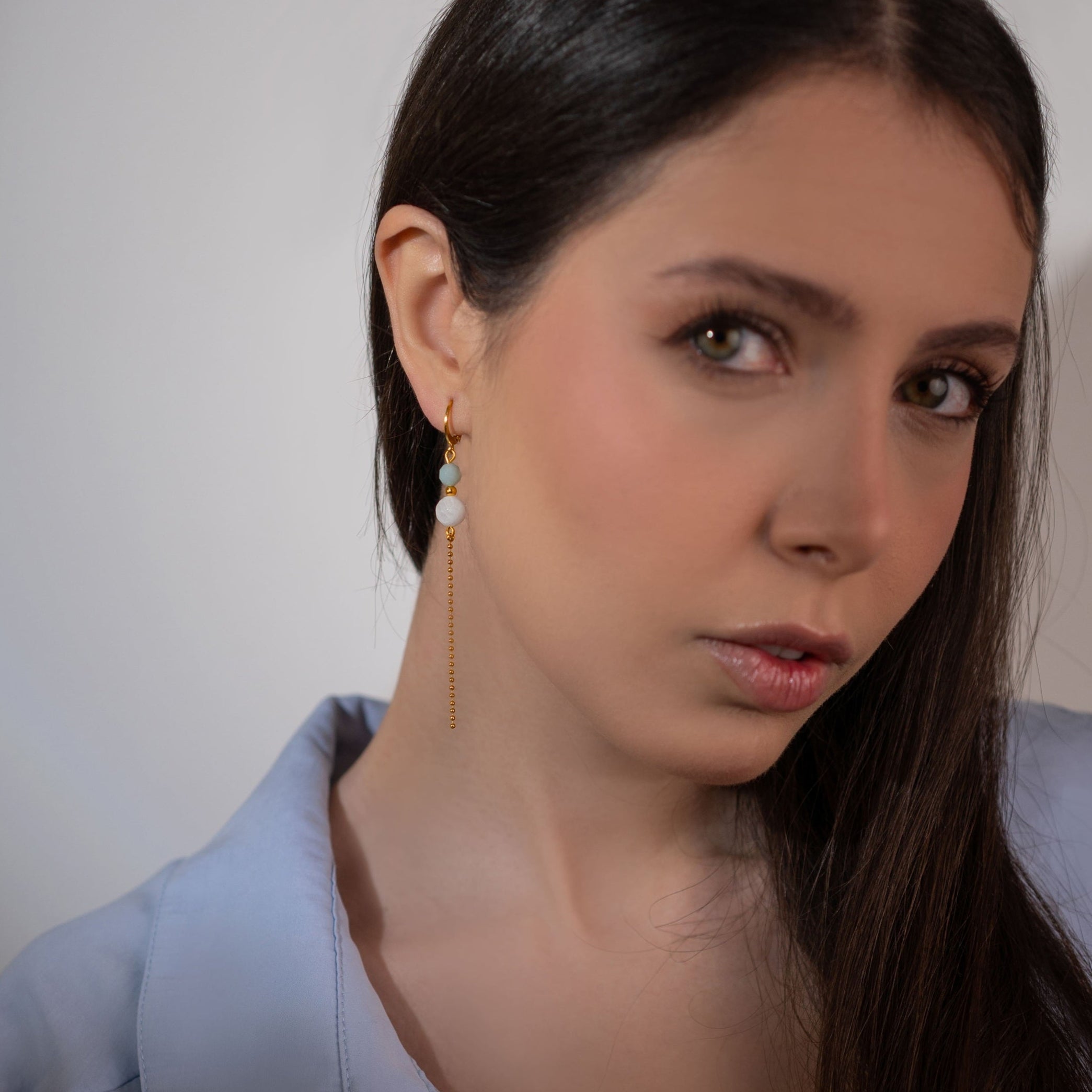 Fines boucles d'oreilles pendantes dorées en perles de pierres naturelles améthyste et mokaïte ocre et chaînette, portées à l'oreille par une femme brune