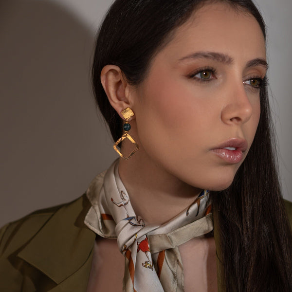 Boucles d'oreilles losanges sur puces en métal martelé doré à l'or fin et perles de jaspe océan vert foncé, portées à l'oreille par une femme brune