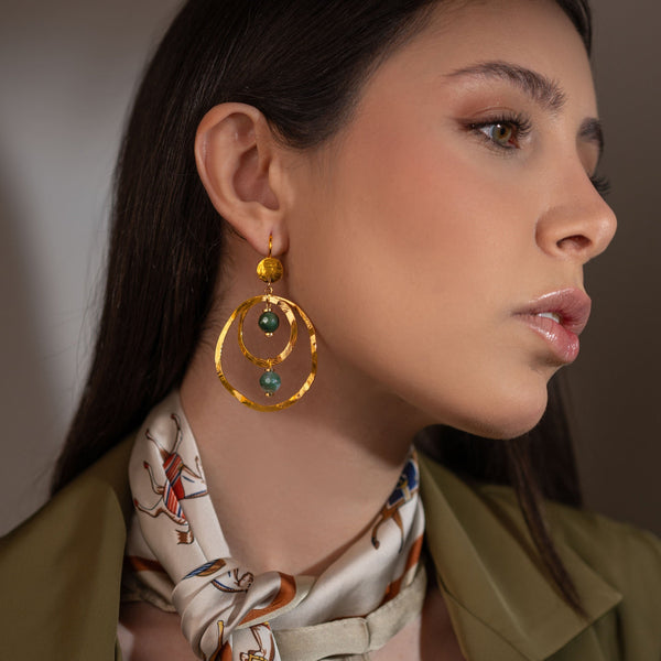 Grandes boucles d'oreilles créoles dorées pendantes longues, style créoles, avec double anneau en métal martelé doré à l'or fin et perles en agate indienne vertes, portées à l'oreille par une femme brune