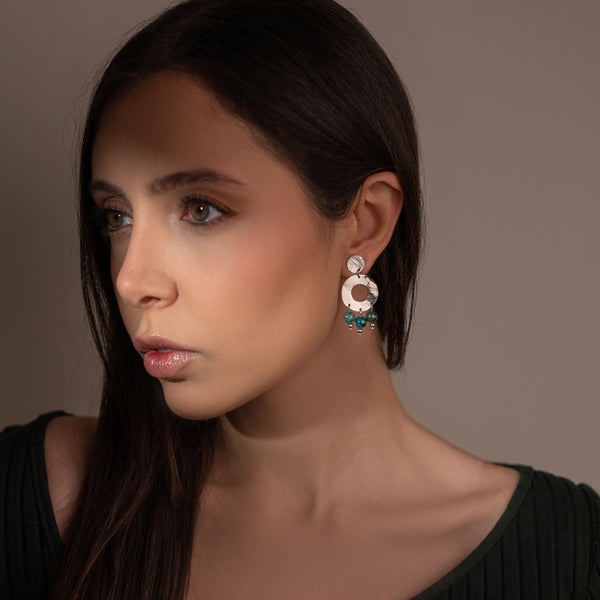 Petites boucles d'oreilles créoles à puces de forme ronde en métal martelé argenté et pierres naturelles de Jaspe océan vert foncé, portées à l'oreille par une femme brune