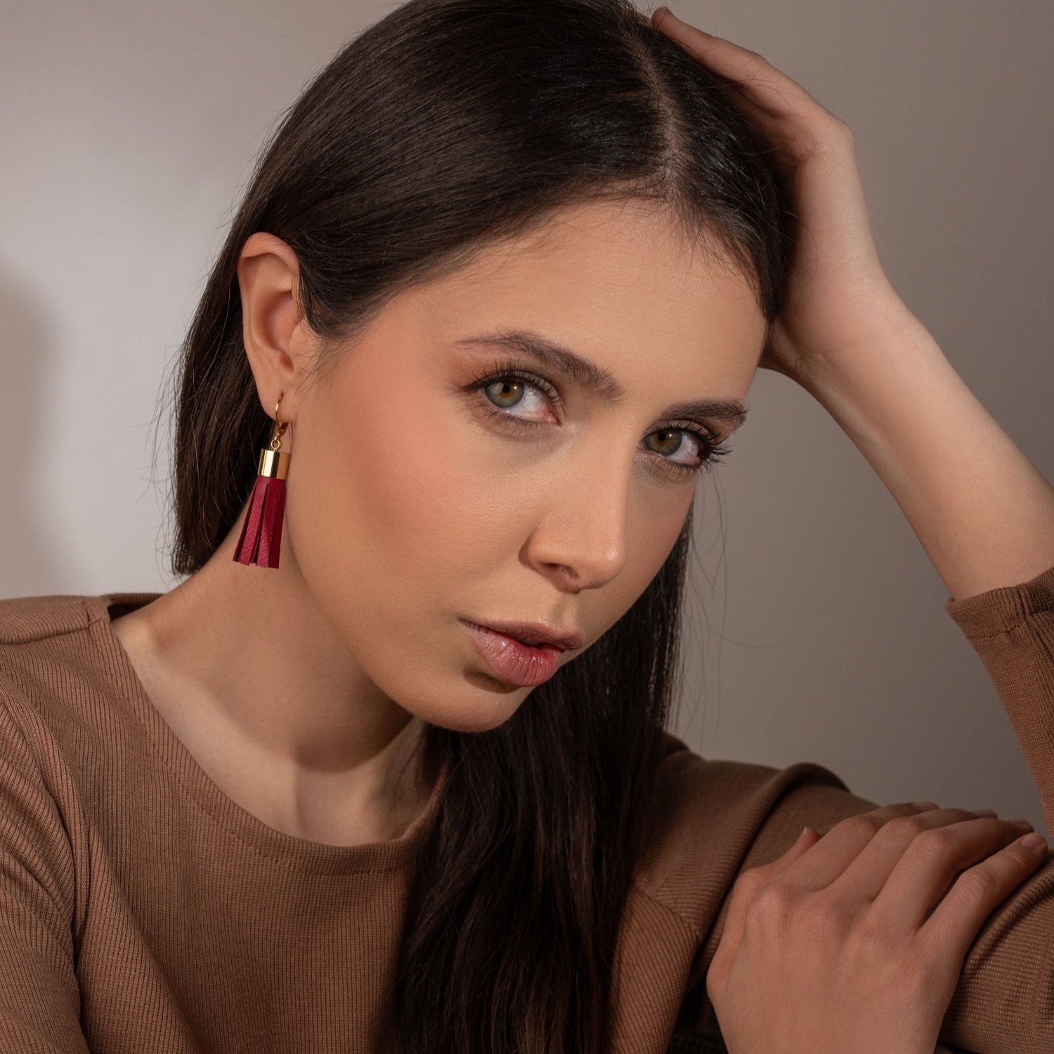 Longues boucles d'oreilles dorées en forme de pompons en cuir pourpre, portées à l'oreille par une femme brune