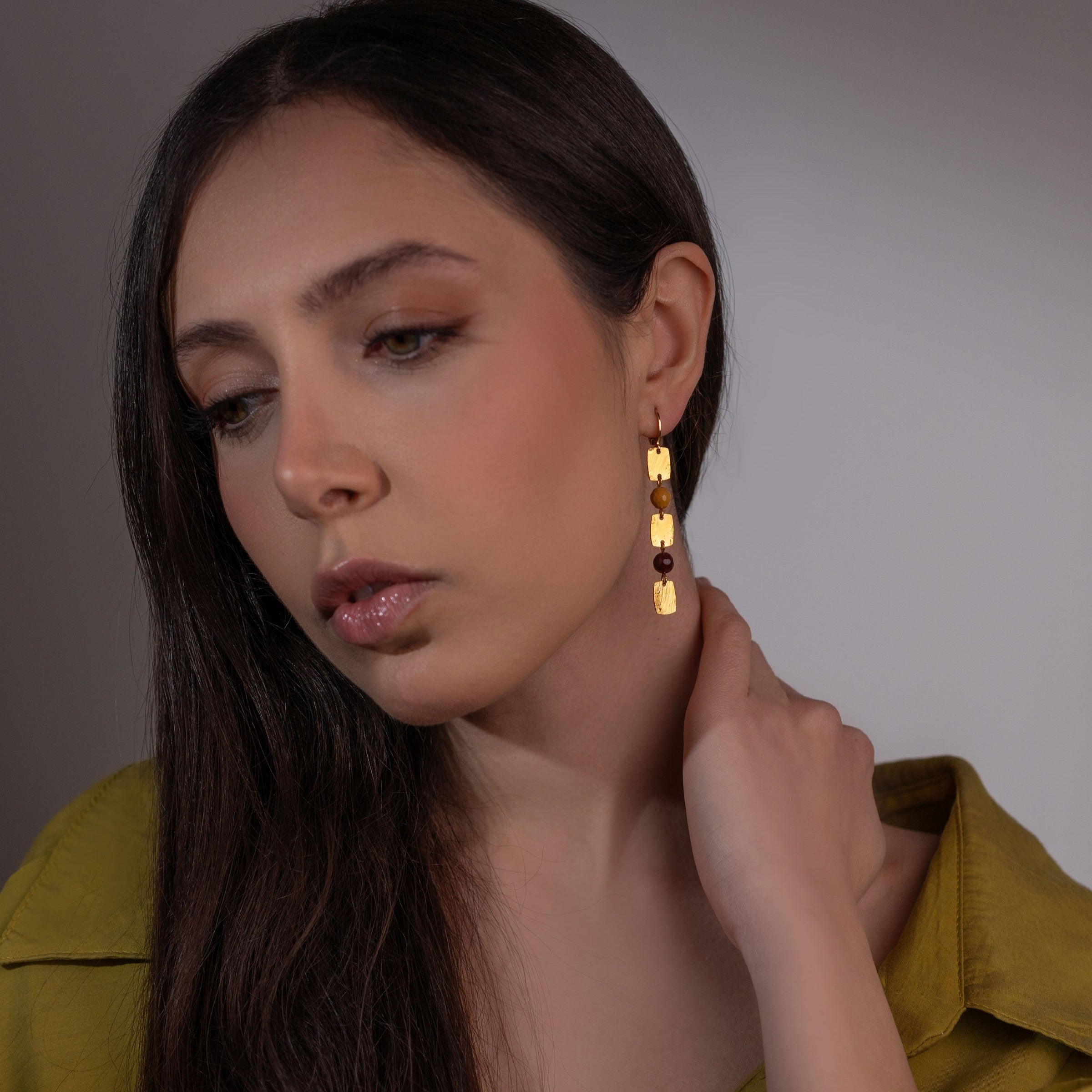 Fines boucles d'oreilles pendantes en chapelet de petits sequins rectangulaires en métal martelé doré à l'or fin et perles de mokaïte ocre et lie de vin, portées à l'oreille 