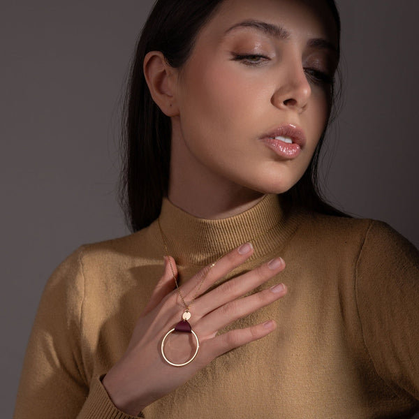 Collier fin dorée avec pendentif grand anneau créole attaché par une fine pièce de cuir pourpre, porté par une femme brune