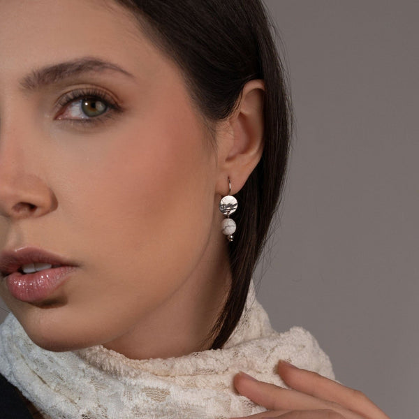 Petites boucles d'oreilles rondes en métal martelé doré à l'or fin avec pendant en perle de mokaïte bordeaux, portées à l'oreille par une femme brune