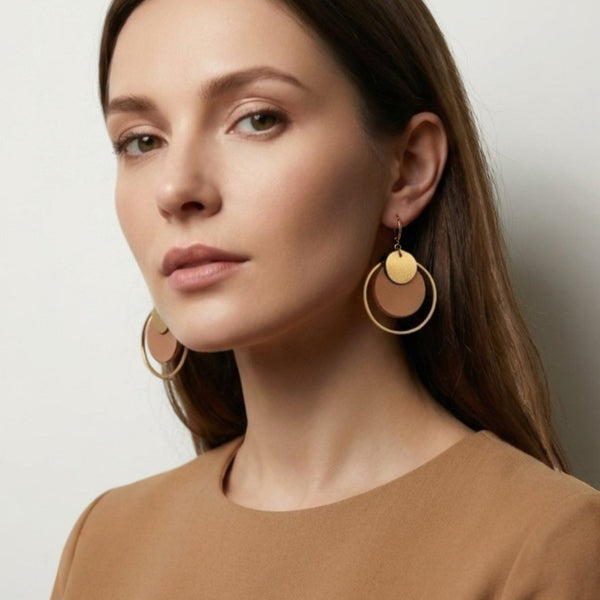 boucles d'oreilles dorées Nune modèle Danaé en cuirs beige amande et doré satiné, portées à l'oreille par une femme brune