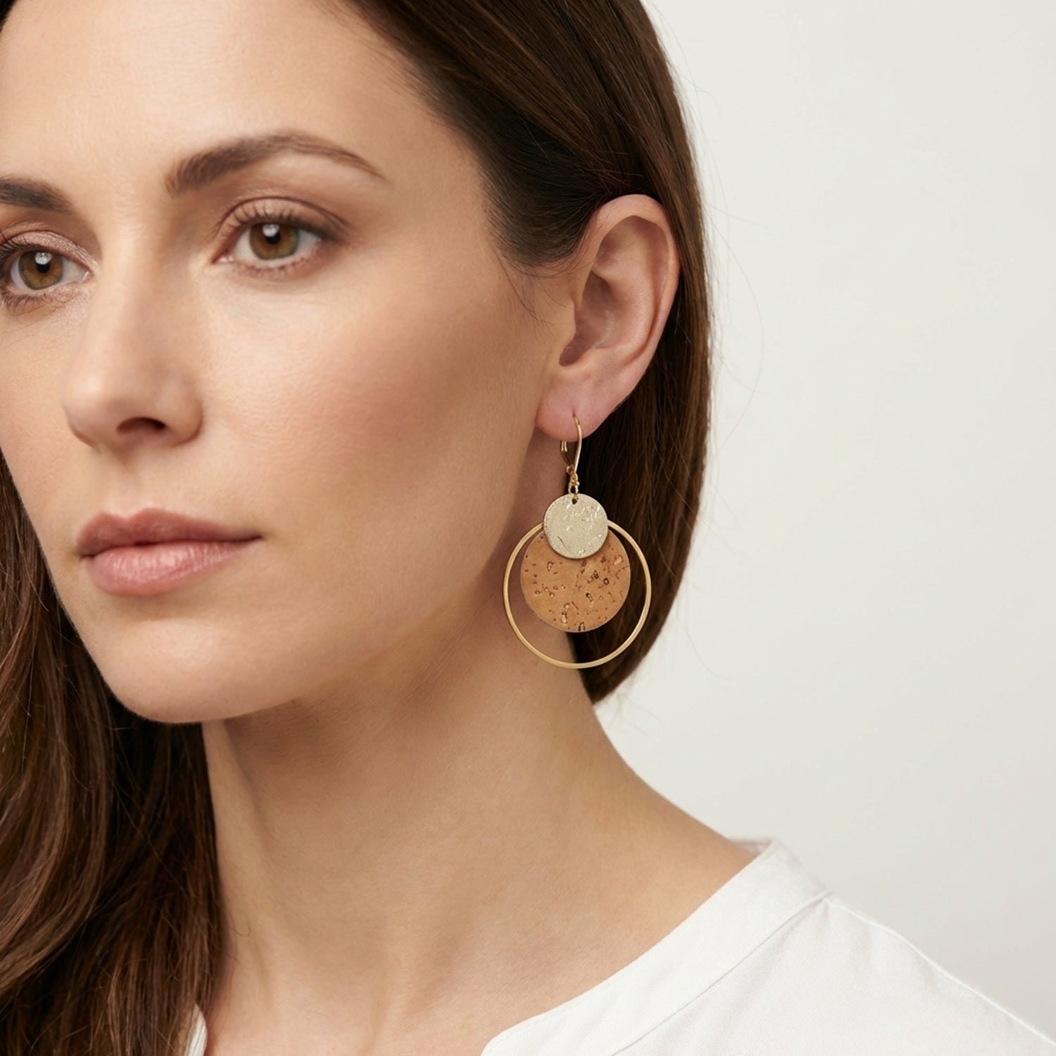 Femme brune portant des Boucles d'oreilles dorées rondes en liège brut et doré antique, soulignées par de grands anneaux dorés