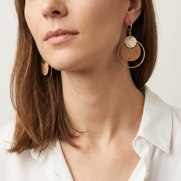 Femme brune portant des Boucles d'oreilles dorées rondes en liège brut et doré antique, soulignées par de grands anneaux dorés, vue du bas du visage