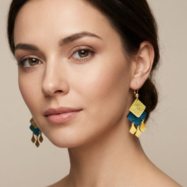 Boucles d'oreilles dorées Diamante en duo de losanges en cuirs doré et bleu nuit métallisé et pendentifs losanges dorés. Forme géométrique, style éthnique. Portée à l'oreille par une femme brune