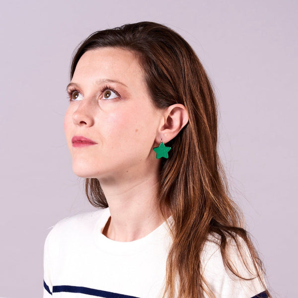 Jeune fille aux longs cheveux bruns avec marinières vue de 3/4 portant les boucles d'oreilles Diva de Nune en forme d'étoile en cuir recyclé vert métallisé, sur mauve