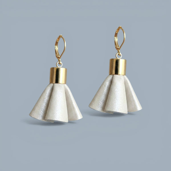 Boucles d'oreilles dorées en pompons frou frou de cuir blanc cassé nacré, debout sur fond gris