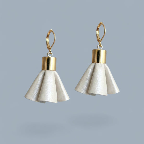 Boucles d'oreilles dorées en pompons frou frou de cuir blanc cassé nacré, debout sur fond gris