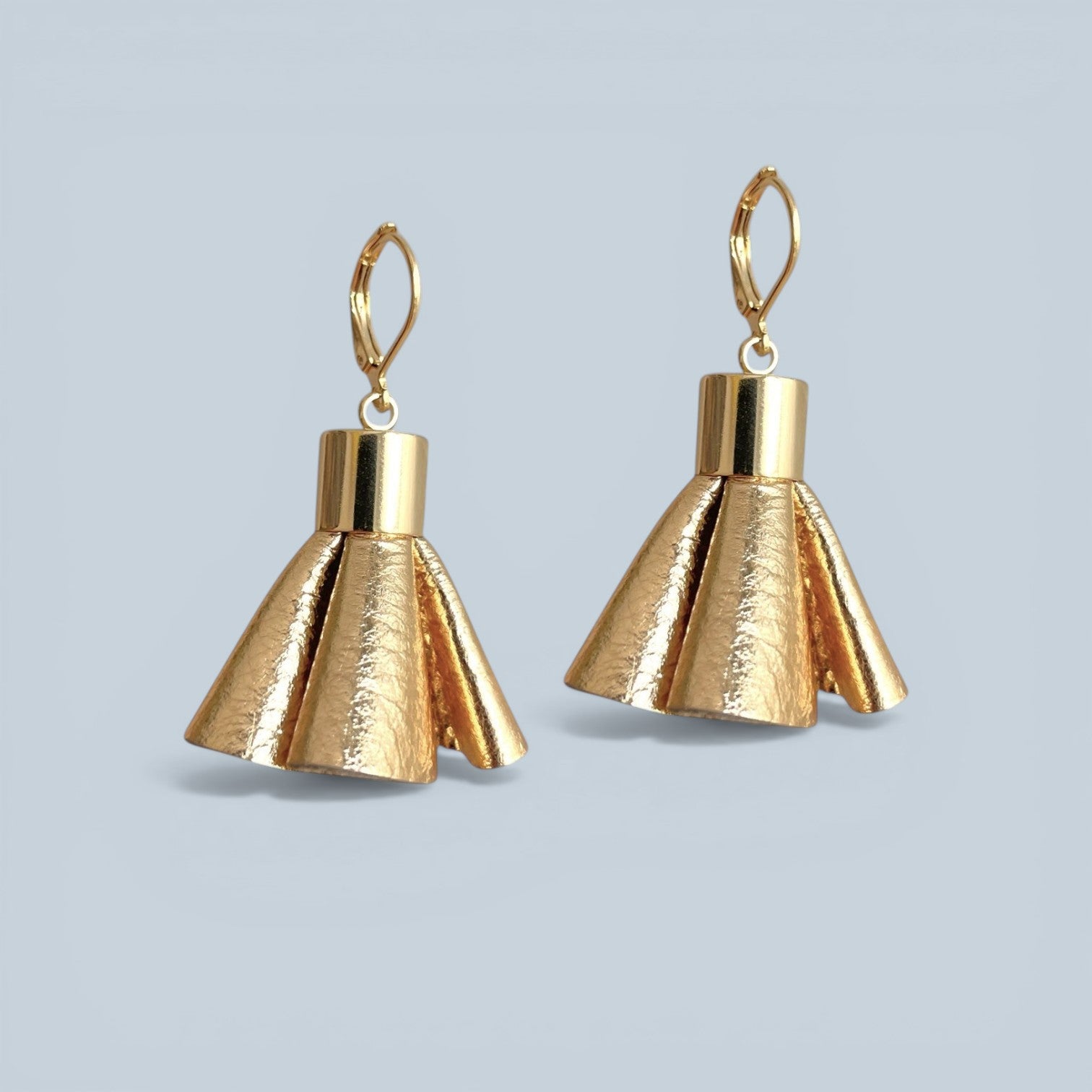 Boucles d'oreilles dorées en pompons frou frou de cuir doré, debout sur fond gris