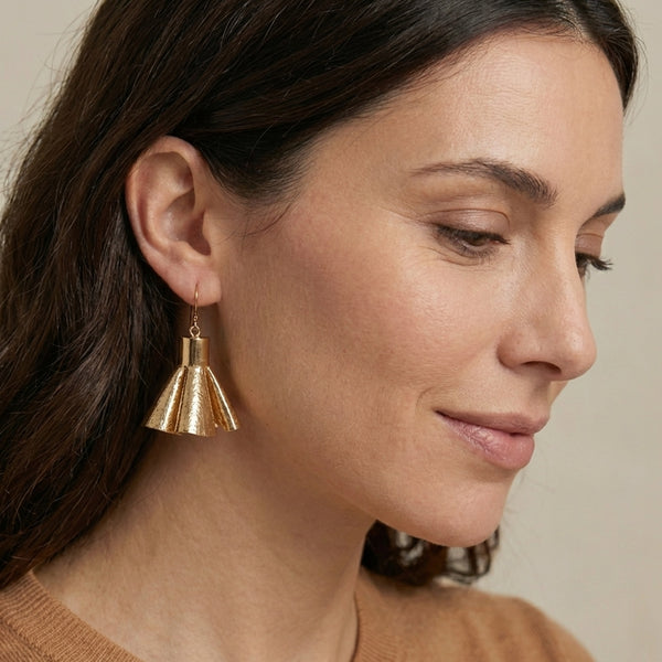 Boucles d'oreilles dorées en pompons frou frou de cuir doré, portées par une femme brune vue de profil
