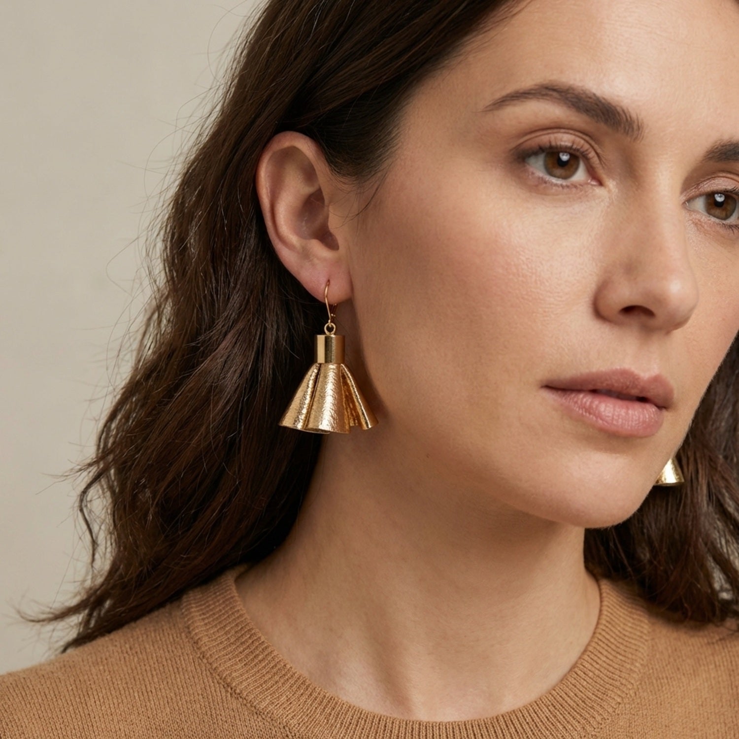 Boucles d'oreilles dorées en pompons frou frou de cuir doré, portées par une femme brune vue de 3/4