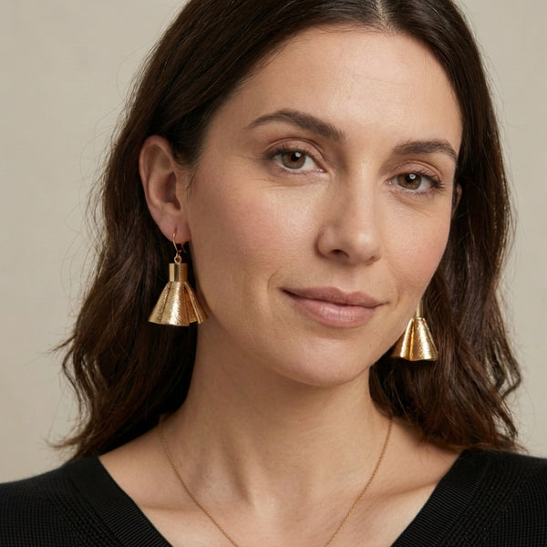 Boucles d'oreilles dorées en pompons frou frou de cuir doré, portées par une femme brune vue de face